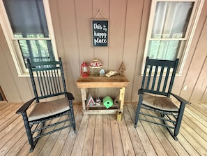 Eine Veranda mit zwei Stühlen, einem kleinen Tisch, einem Schild und einem Vogelhäuschen.