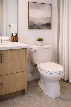 Une salle de bain moderne comprenant des toilettes, un lavabo avec des articles de toilette, un meuble et un tableau encadré accroché au mur.