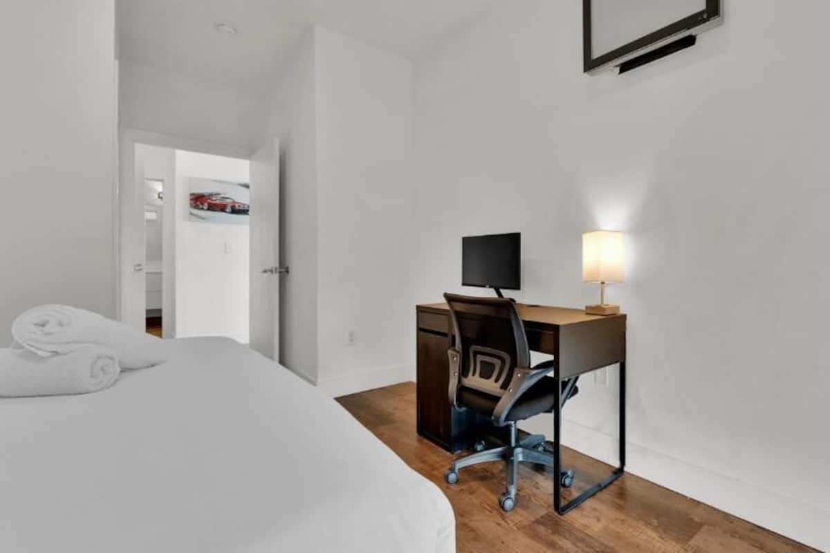 Une chambre d’hôtel comprenant un lit, un bureau avec un ordinateur et une lampe, ainsi qu’une porte donnant sur une autre pièce.