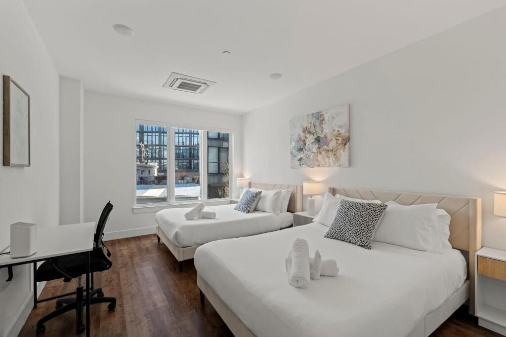 A hotel room with two beds, a desk, and a large window.