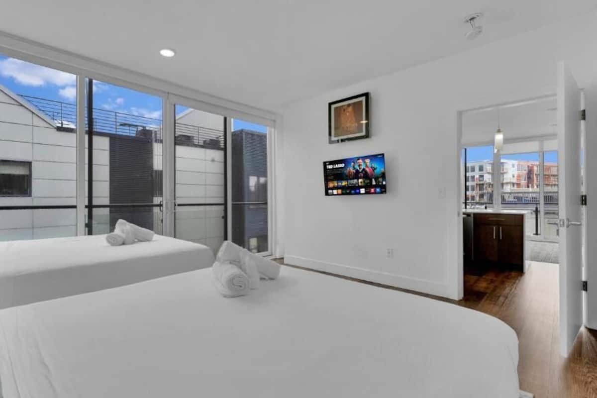 Une chambre d’hôtel moderne avec deux lits, une télévision et un balcon offrant une vue sur la ville.