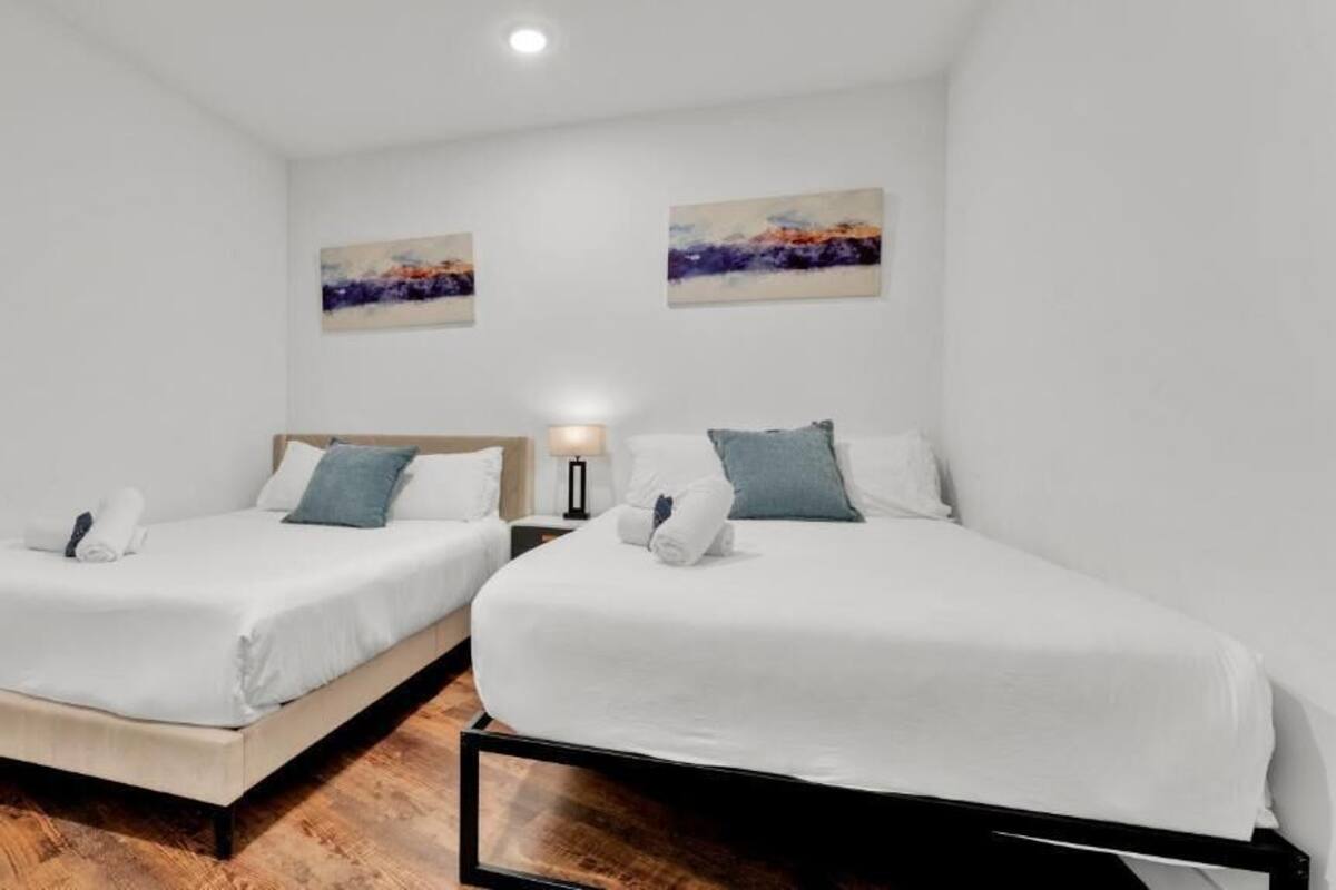 Deux lits simples avec du linge de lit blanc, des têtes de lit en bois et une table de chevet avec une lampe.