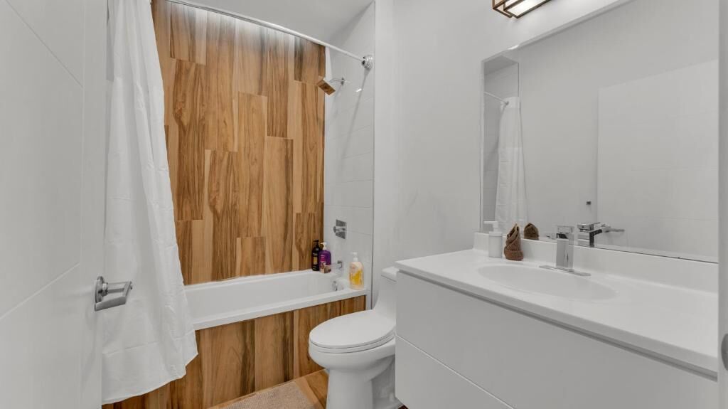 A modern bathroom with a wooden shower wall, a white toilet, and a large mirror above the sink.