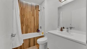 A modern bathroom with a wooden shower wall, a white toilet, and a large mirror above the sink.