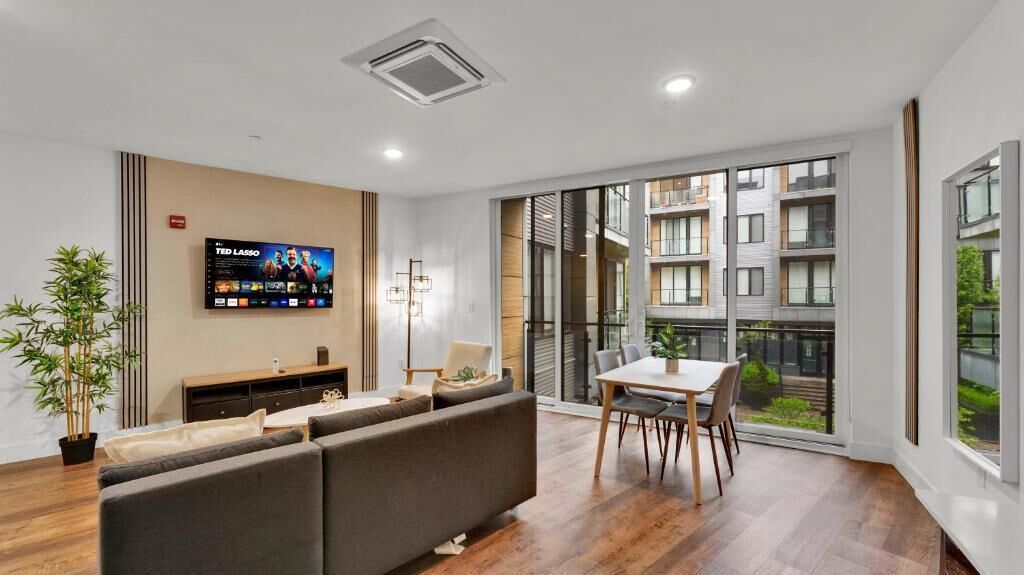 A modern living room with a sofa, TV, dining table, and large windows.