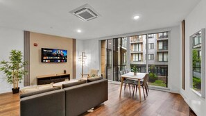 A modern living room with a sofa, TV, dining table, and large windows.