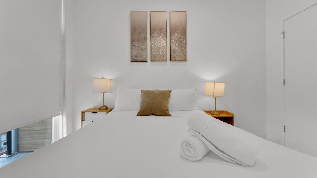 A modern hotel room with a large bed, two bedside tables, a headboard, and a wall-mounted artwork.
