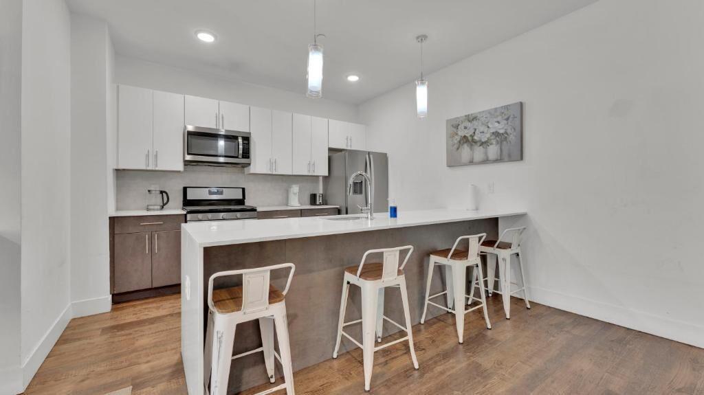 A modern kitchen with white cabinets, stainless steel appliances, a wooden countertop, and three white bar stools.