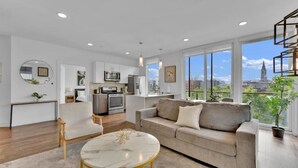 A modern apartment with a living room, kitchen, and large windows offering a city view. - Apartmint at Liberty A Philadelphia (Philadelphia)
