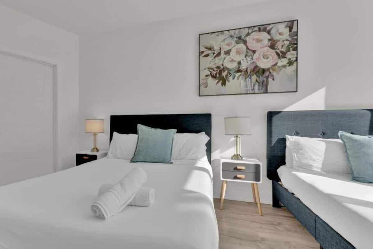 A hotel room with a large bed, two bedside tables, a nightstand, a painting on the wall, and a door.