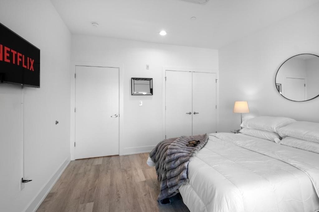 A bedroom with a bed, a TV mounted on the wall, a mirror, and a door.