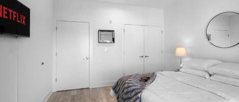 A bedroom with a bed, a TV mounted on the wall, a mirror, and a door.