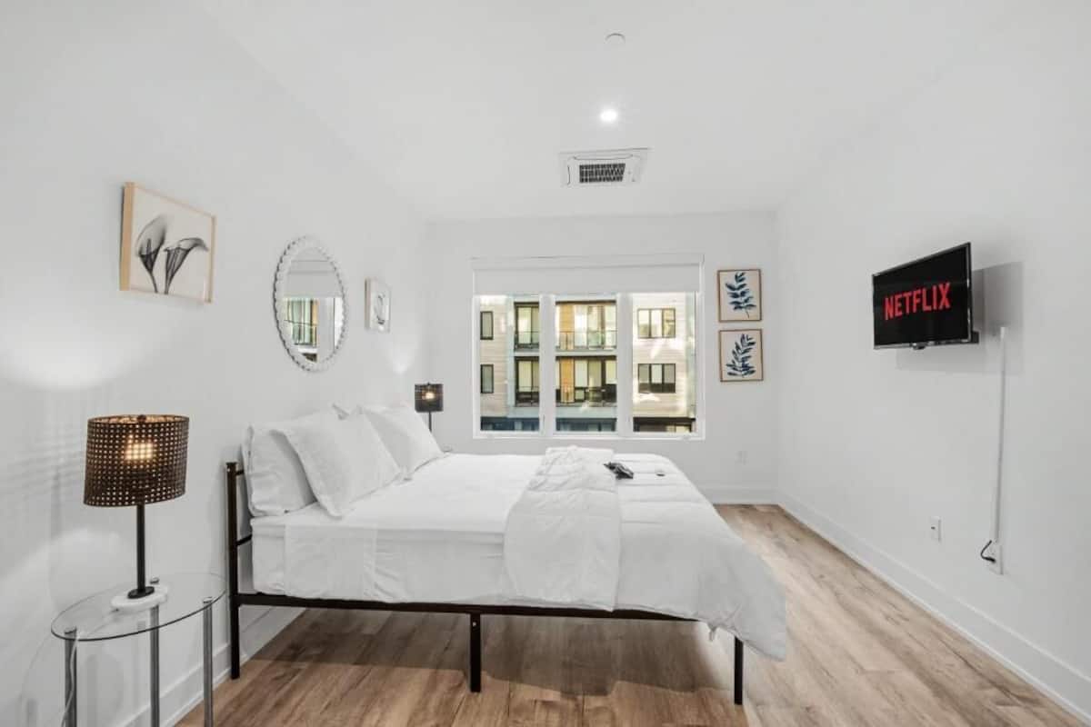 A bedroom with a bed, a TV, a window with a view, and a lamp.