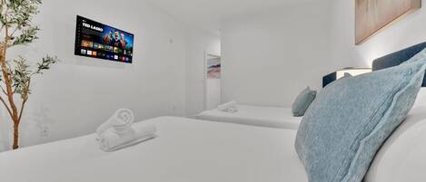 A modern hotel room with a flat-screen TV, two beds, a plant, and a painting on the wall.