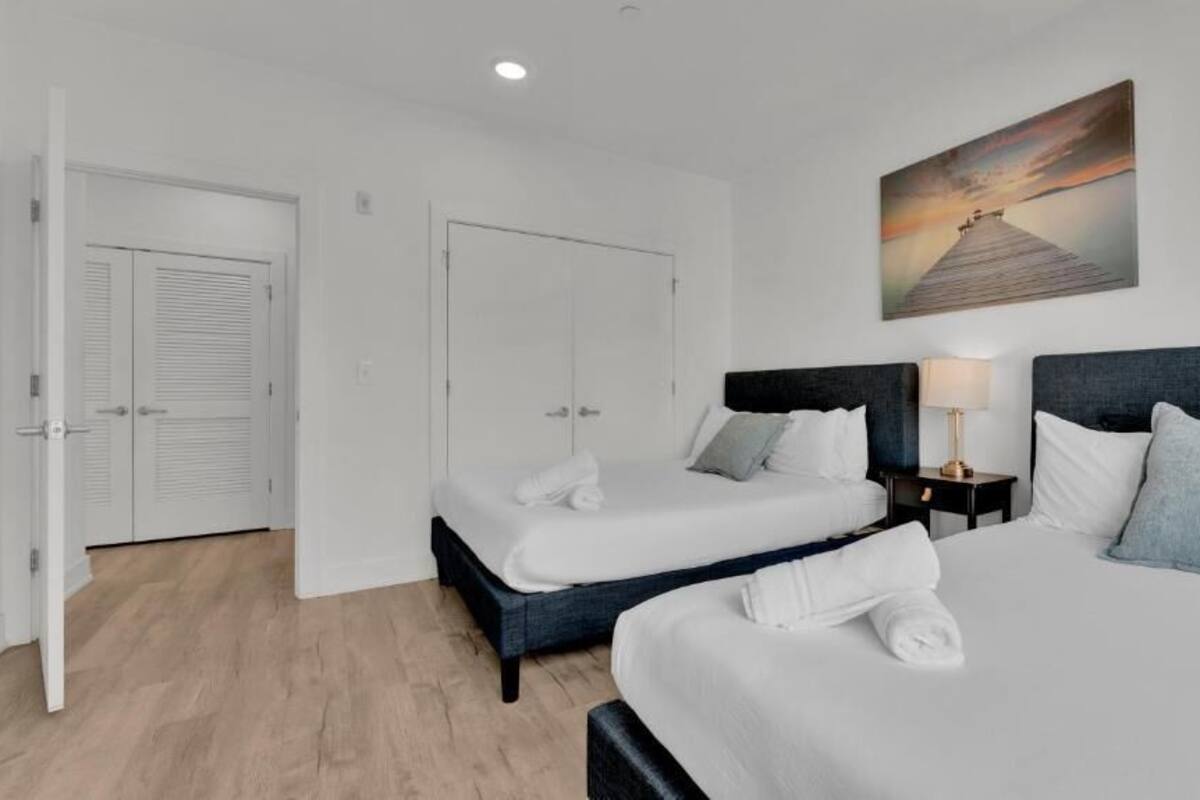 A hotel room with two beds, a painting on the wall, and a nightstand with a lamp.