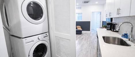 A laundry area with stacked washers and dryers, a kitchen with a sink, and a living area with a sofa.
