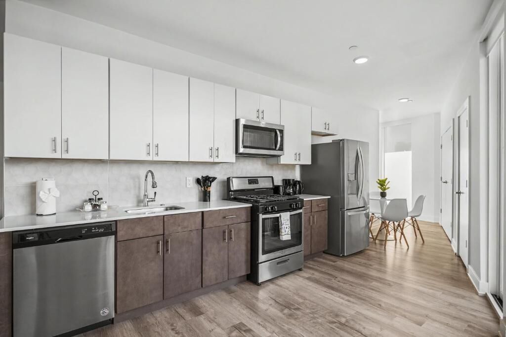 A modern kitchen with white cabinets, stainless steel appliances, and a wooden floor.