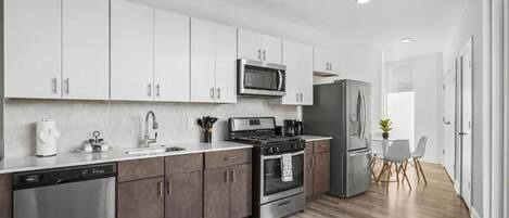 A modern kitchen with white cabinets, stainless steel appliances, and a wooden floor.