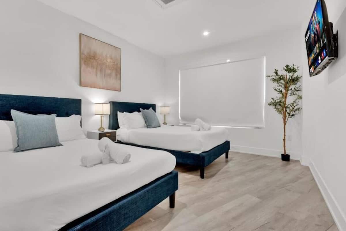 A hotel room with two beds, a large window, a flat-screen TV, and a plant.