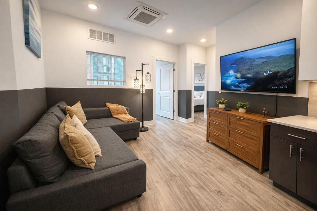 Ein modernes Wohnzimmer mit einem Ecksofa, einem Flachbildfernseher, Holzausbau und einer Tür zu einem weiteren Raum.