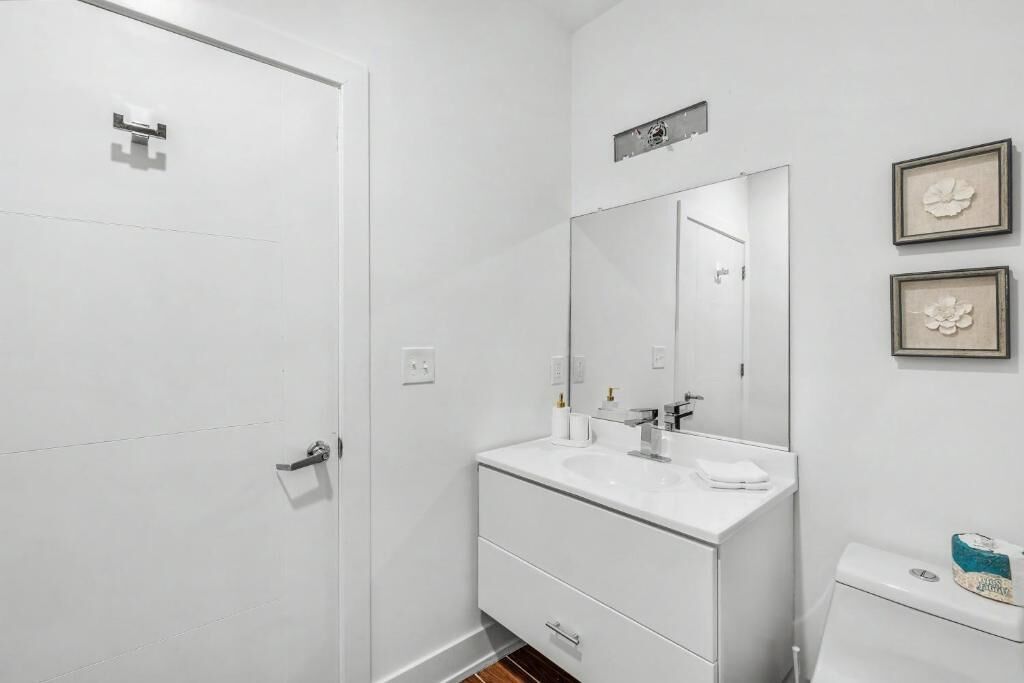 Un baño con lavamanos blanco, espejo e inodoro. Hay cuadros enmarcados en la pared.
