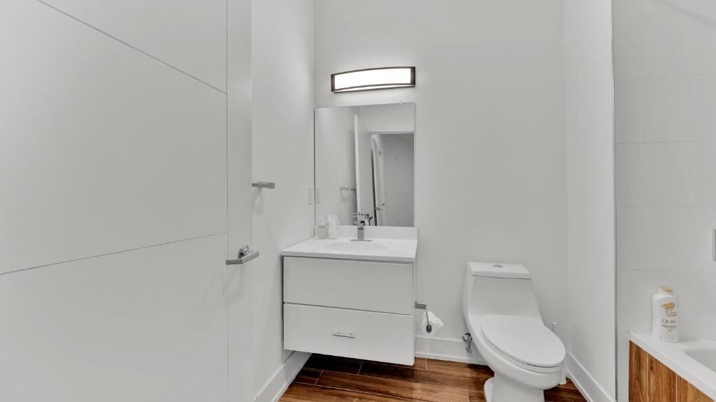 A small, modern bathroom with a white sink, mirror, and toilet.