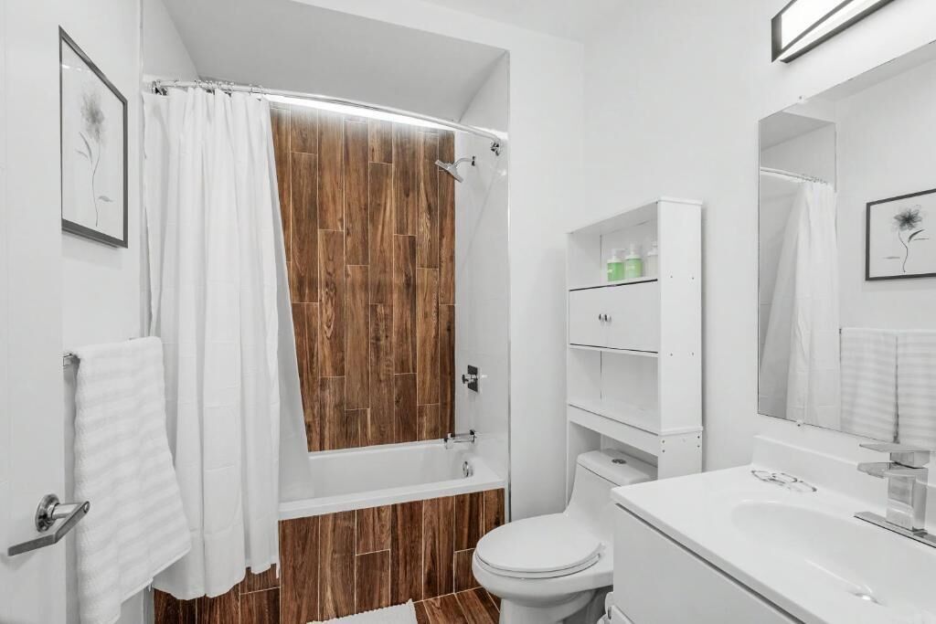 Une salle de bain avec une cabine de douche en bois, des toilettes blanches, un lavabo blanc et un miroir au-dessus du lavabo.