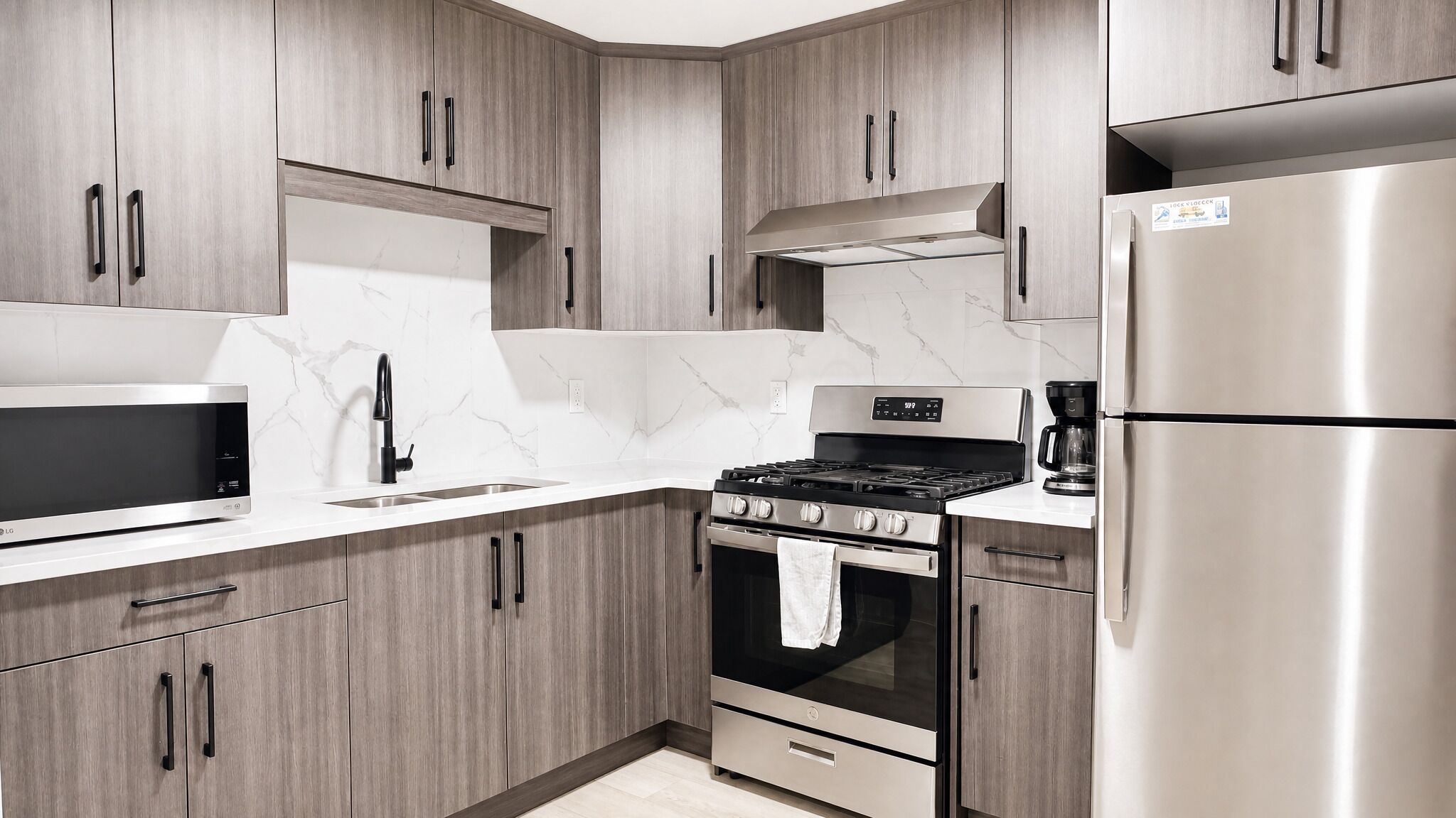 A modern kitchen with wooden cabinets, a stainless steel refrigerator, a built-in oven, and a microwave.