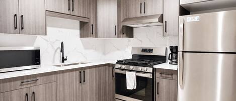A modern kitchen with wooden cabinets, a stainless steel refrigerator, a built-in oven, and a microwave.