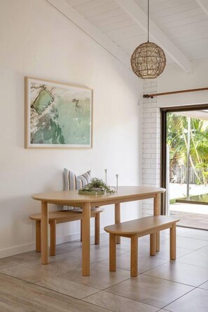 A dining area with a wooden table and bench, a hanging light fixture, and a framed abstract painting on the wall.