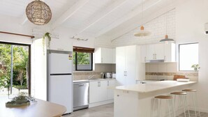 Eine moderne Küche mit weißen Schränken, einer zentralen Kochinsel inklusive Barhocker, einem Geschirrspüler und einem Kühlschrank.