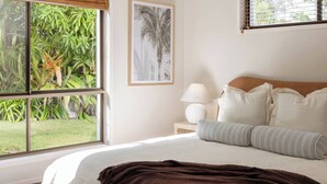 A bedroom with a large window, a bed with white bedding, a brown throw blanket, and a framed picture on the wall.