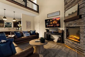 A modern living room with a fireplace, a television displaying a cabin, and a sign above stating 'The Gathering Place'. - 2 min drive to Silver Dollar City, 4BR/4BA Family Friendly Retreat (Branson)