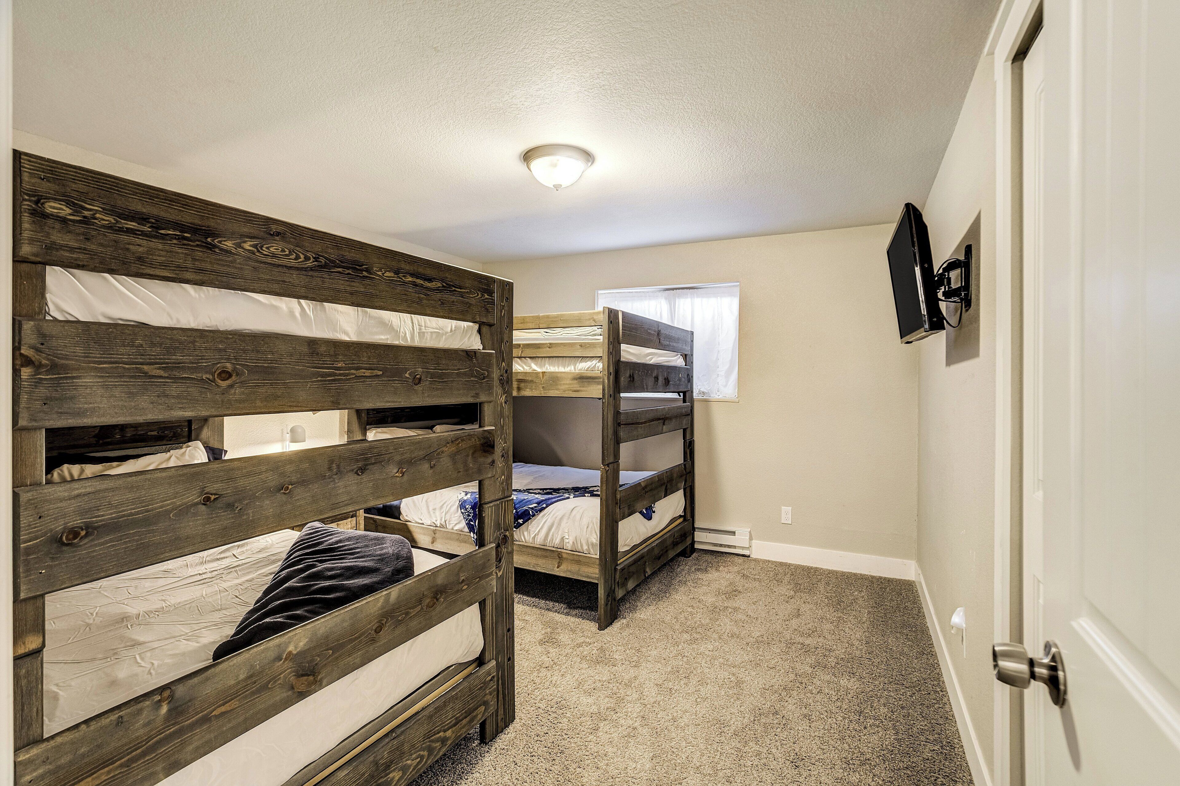 A bedroom with two bunk beds, a window with sheer curtains, a wall-mounted TV, and a door with a silver handle.