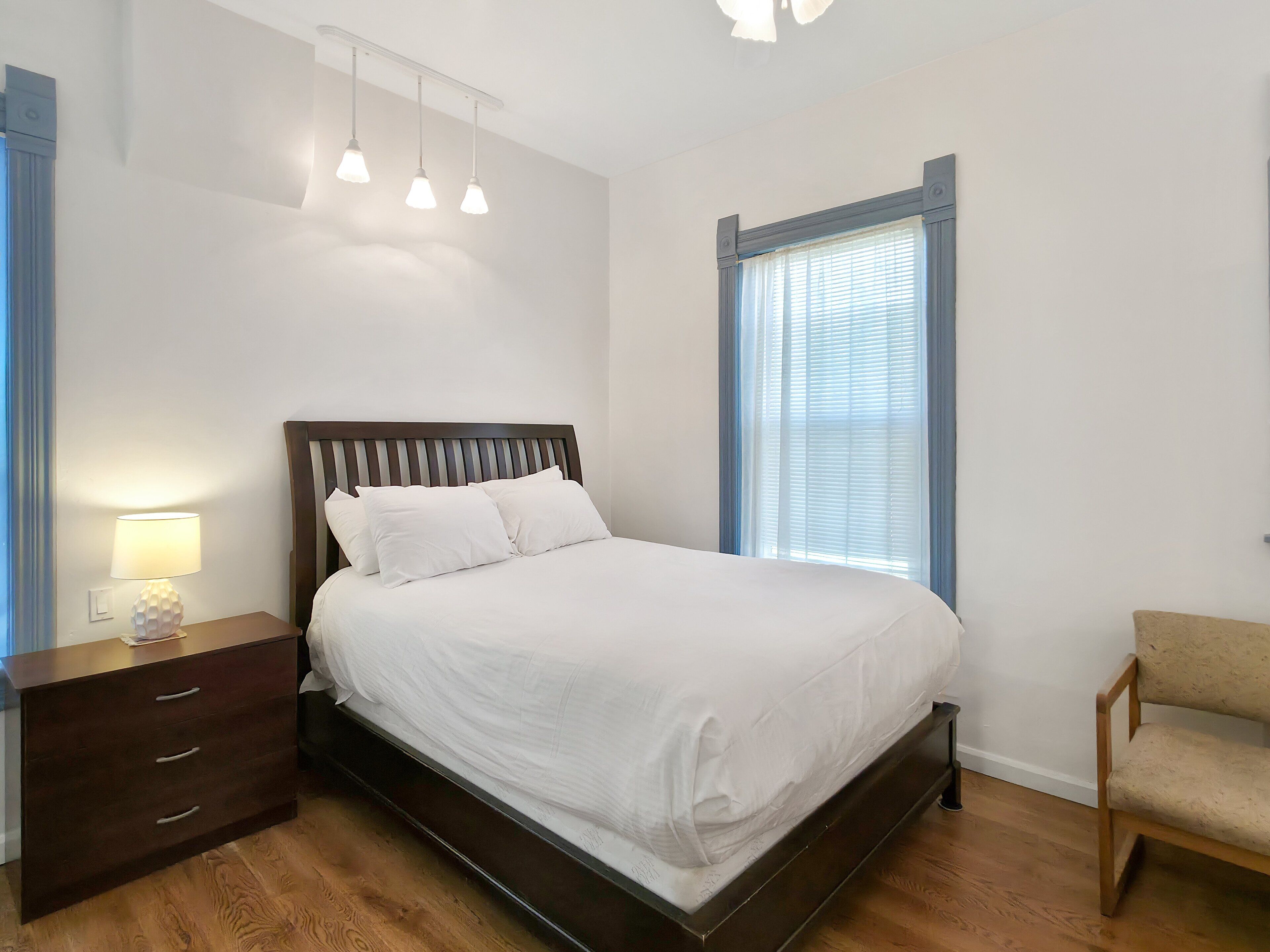 A bedroom with a bed, bedside table, lamp, and a chair.