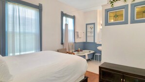 Ein Schlafzimmer mit Bett, einem kleinen Tisch, einem Stuhl, einer Badewanne und einem Schminktisch mit Spiegel.