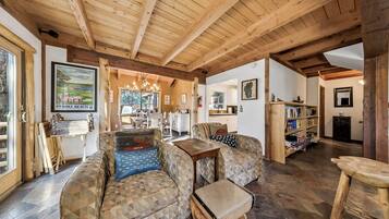 A cozy living room with a wooden ceiling, a sofa with patterned cushions, a small wooden table, and a bookshelf.