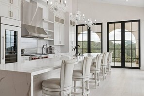 Una cocina moderna con una isla central, armarios blancos y un comedor con sillas blancas.