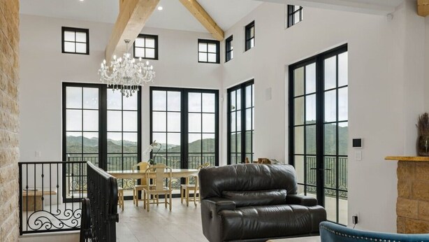 Un vaste espace de vie comprenant un canapé en cuir, une table à manger et des chaises, de grandes fenêtres offrant une vue sur les montagnes et un lustre.