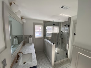 Une salle de bain dotée d’une douche à parois de verre, d’un double lavabo avec un plan de toilette en marbre et d’un grand miroir.