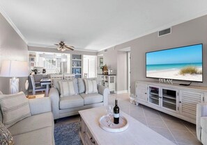Ein modernes Wohnzimmer mit Sofa, Couchtisch, Fernseher und Blick auf den Strand.