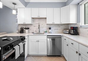 Une cuisine moderne avec des meubles blancs, un lave-vaisselle en acier inoxydable, une cuisinière noire et une machine à café.