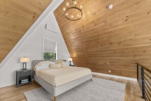 Ein Schlafzimmer mit schrägem Dach, einem Bett, Nachttischlampen, einem Fenster und einer Chandelier.