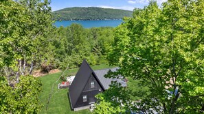 Ein Haus mit dunklem Dach, umgeben von üppigen grünen Bäumen und einem See im Hintergrund.