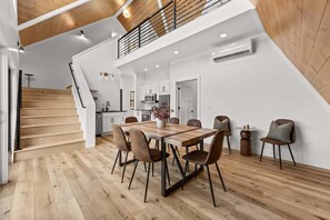 Eine moderne Küche mit weißen Schränken, ein Essbereich mit einem Holztisch und -stühlen sowie eine Treppe mit Holzbodenstufen.