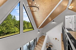 Ein modernes Interieur mit Holzboden, großen Fenstern, einer Treppe und Blick auf Grünflächen.