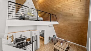 A modern loft-style apartment with a kitchen, dining area, and a loft bedroom with a balcony. - Fernwood: modern cabin with hot tub, putting green, pickleball (Hammondsport)