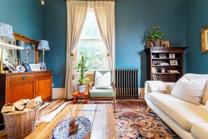 A room with a sofa, a chair, a wooden cabinet, a radiator, and a window with curtains. - Renovated Spacious 3-Bed Newark Home with High Ceilings (Newark-on-Trent)
