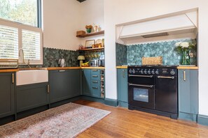A kitchen with dark cabinets, a stove, a window with blinds, and a patterned rug. - Renovated Spacious 3-Bed Newark Home with High Ceilings (Newark-on-Trent)