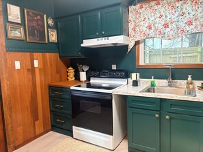 A kitchen with a stove, oven, and sink, wooden cabinets, and a window with a floral curtain.